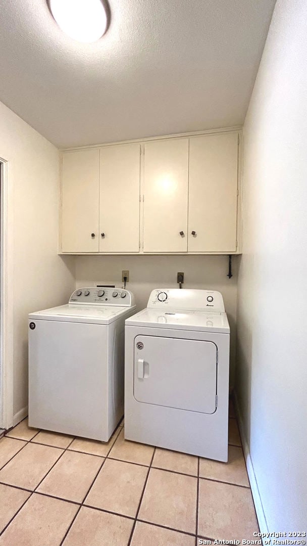 washroom with a textured ceiling, cabinets, light tile patterned floors, and independent washer and dryer