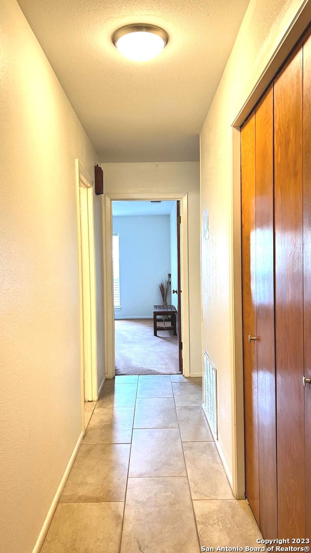 hallway featuring a textured ceiling and light tile patterned floors