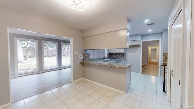 kitchen featuring sink, decorative backsplash, light stone counters, kitchen peninsula, and light hardwood / wood-style flooring