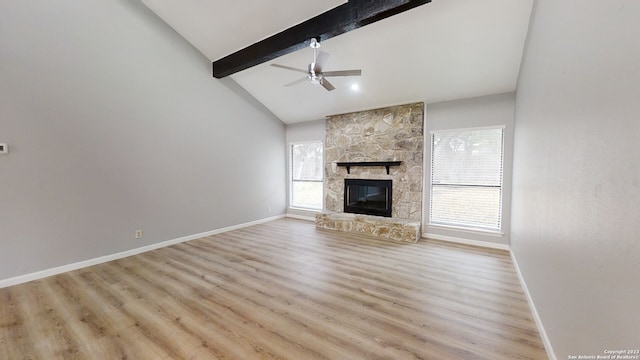 unfurnished living room with a stone fireplace, plenty of natural light, lofted ceiling with beams, and ceiling fan