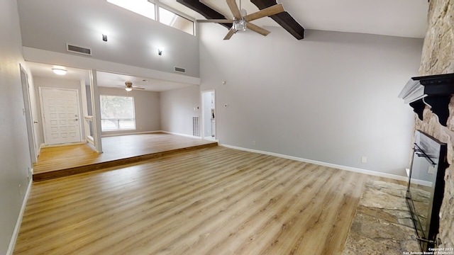 unfurnished living room featuring beam ceiling, high vaulted ceiling, light wood-type flooring, ceiling fan, and a fireplace