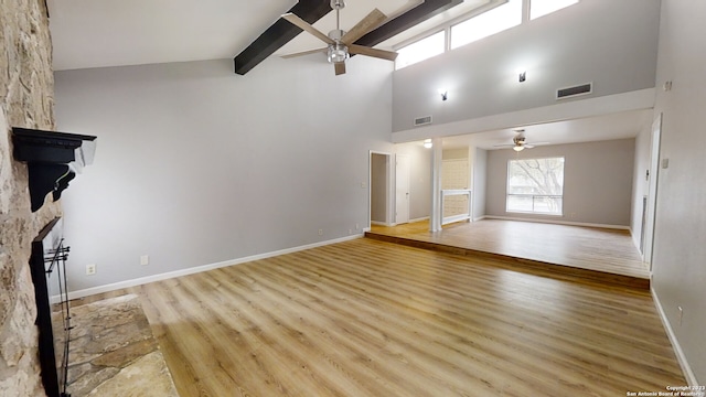 unfurnished living room featuring a stone fireplace, high vaulted ceiling, light hardwood / wood-style flooring, ceiling fan, and beam ceiling