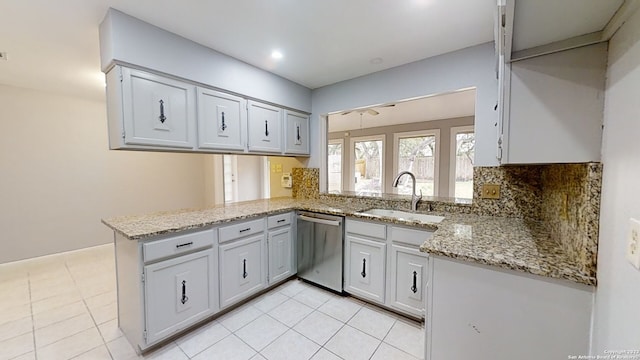 kitchen featuring tasteful backsplash, dishwasher, sink, light stone counters, and kitchen peninsula