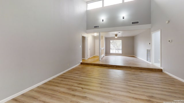 unfurnished living room featuring ceiling fan, a towering ceiling, and light hardwood / wood-style floors