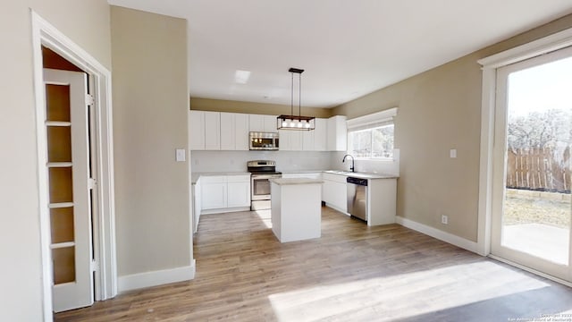 kitchen featuring white cabinetry, hanging light fixtures, light wood-type flooring, appliances with stainless steel finishes, and a kitchen island