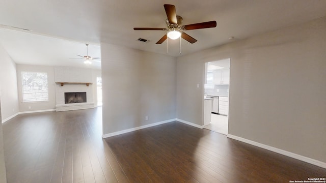 unfurnished living room featuring ceiling fan, dark hardwood / wood-style floors, and a brick fireplace