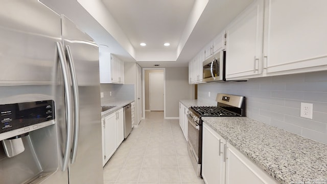 kitchen with white cabinetry, a tray ceiling, light stone countertops, and appliances with stainless steel finishes