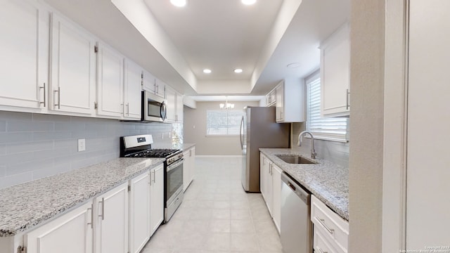 kitchen featuring sink, light stone counters, a raised ceiling, stainless steel appliances, and white cabinets