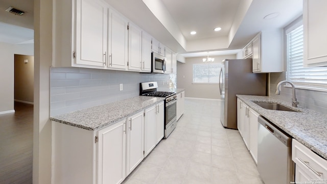 kitchen featuring appliances with stainless steel finishes, a raised ceiling, sink, and white cabinets