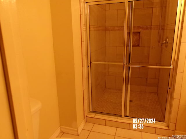 bathroom featuring toilet, a shower with door, and tile patterned floors