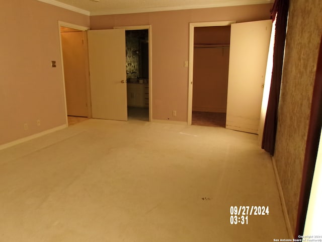 unfurnished bedroom featuring ensuite bath, a spacious closet, a closet, light colored carpet, and crown molding