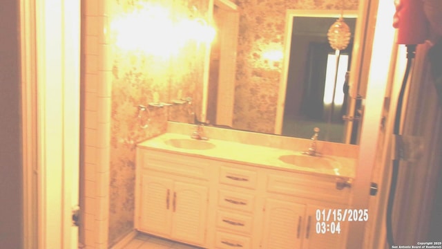 bathroom featuring wallpapered walls, a sink, and double vanity