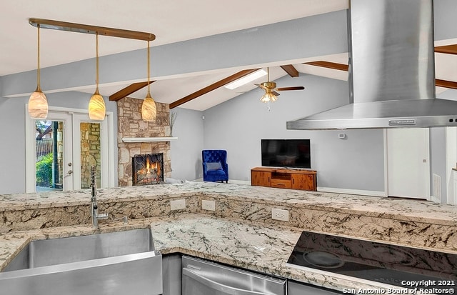 kitchen featuring vaulted ceiling with beams, wall chimney range hood, hanging light fixtures, a stone fireplace, and sink