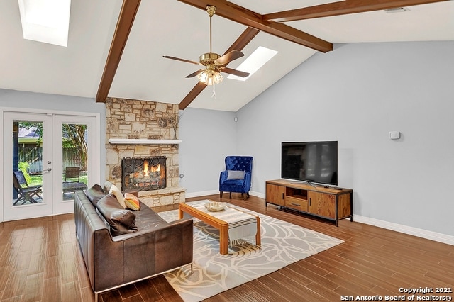 living room featuring beamed ceiling, a stone fireplace, french doors, a skylight, and wood-type flooring