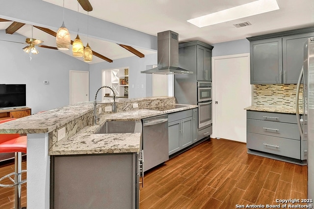 kitchen with appliances with stainless steel finishes, wall chimney range hood, pendant lighting, gray cabinets, and ceiling fan