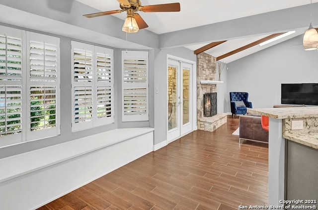 interior space with a stone fireplace, hardwood / wood-style floors, ceiling fan, and vaulted ceiling with beams