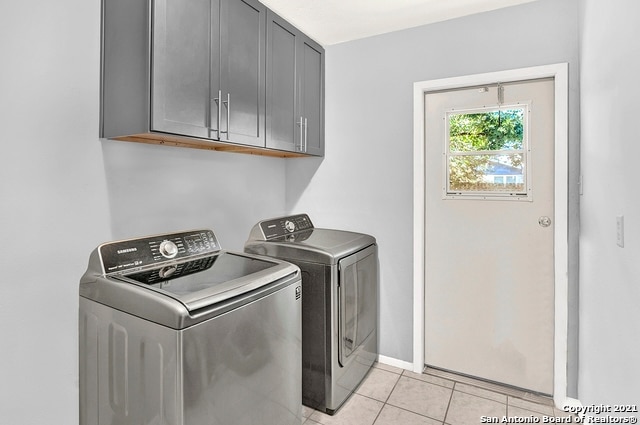 laundry area featuring washing machine and dryer, cabinets, and light tile patterned floors