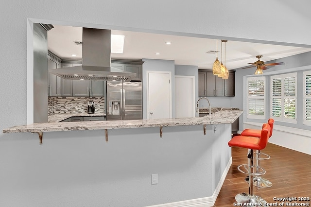 kitchen featuring island range hood, stainless steel fridge, decorative light fixtures, decorative backsplash, and ceiling fan