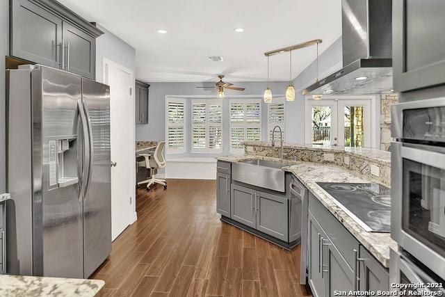 kitchen with stainless steel appliances, wall chimney range hood, sink, gray cabinets, and ceiling fan