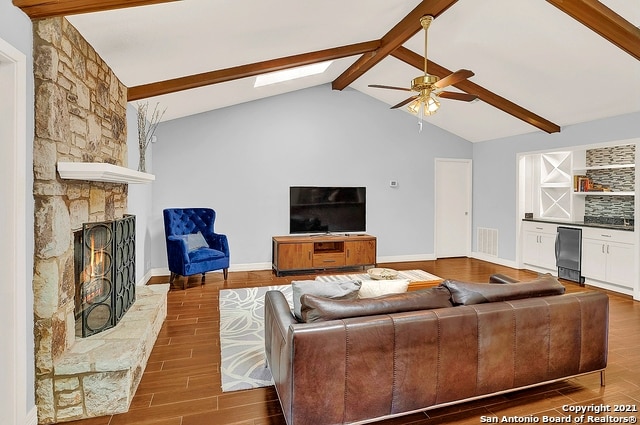 living room with a fireplace, wood-type flooring, ceiling fan, a skylight, and beam ceiling