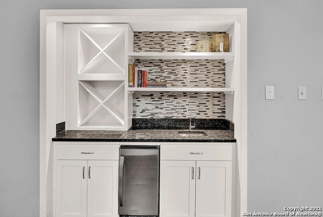 bar featuring white cabinets, backsplash, fridge, and dark stone countertops