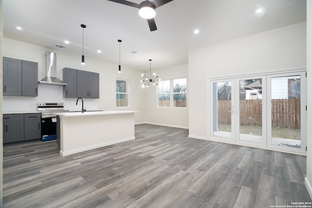 kitchen featuring a kitchen island with sink, ceiling fan with notable chandelier, wall chimney range hood, hanging light fixtures, and electric range