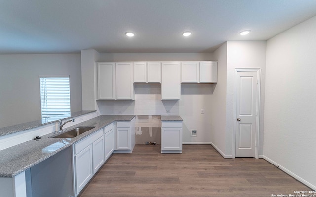 kitchen featuring kitchen peninsula, sink, light stone counters, light wood-type flooring, and white cabinets