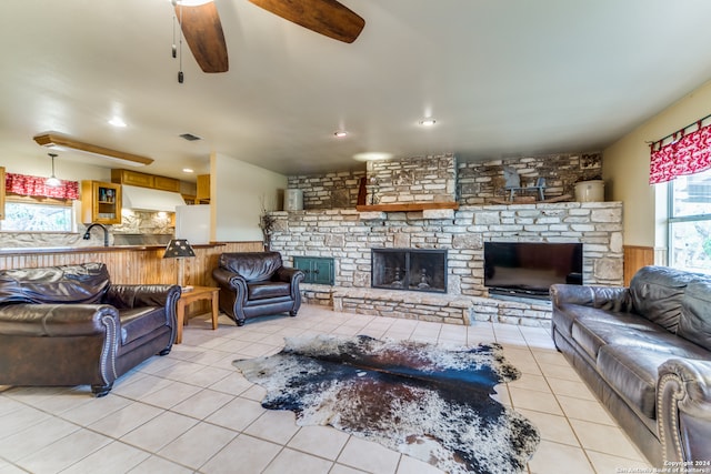 tiled living room with a stone fireplace, sink, and ceiling fan