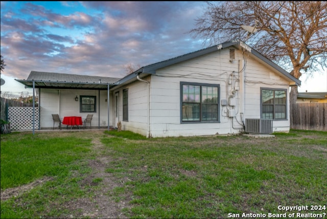 back house at dusk with central AC unit and a lawn