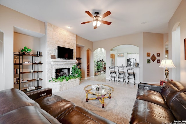 living room featuring ceiling fan, carpet, and a stone fireplace