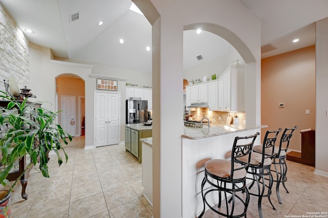 kitchen with light tile patterned floors, stainless steel fridge with ice dispenser, tasteful backsplash, high vaulted ceiling, and white cabinetry