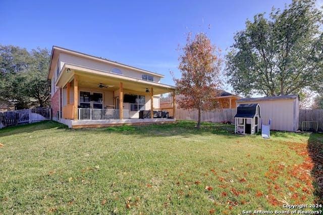 rear view of house with ceiling fan, a lawn, and a shed