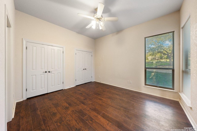 unfurnished bedroom featuring dark wood finished floors, ceiling fan, baseboards, and multiple closets