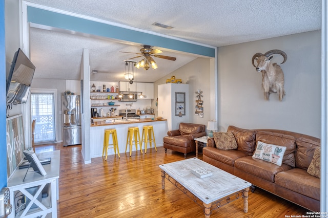 living room featuring lofted ceiling with beams, light hardwood / wood-style floors, ceiling fan, and a textured ceiling