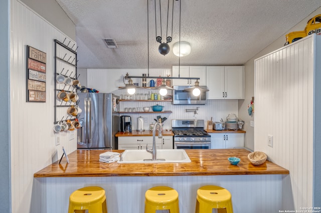 kitchen with a breakfast bar, stainless steel appliances, a textured ceiling, and decorative light fixtures