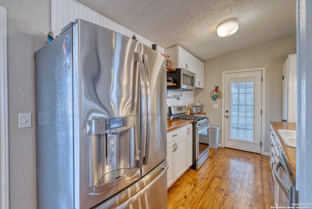 kitchen featuring stainless steel appliances, butcher block counters, light wood-type flooring, a textured ceiling, and white cabinets