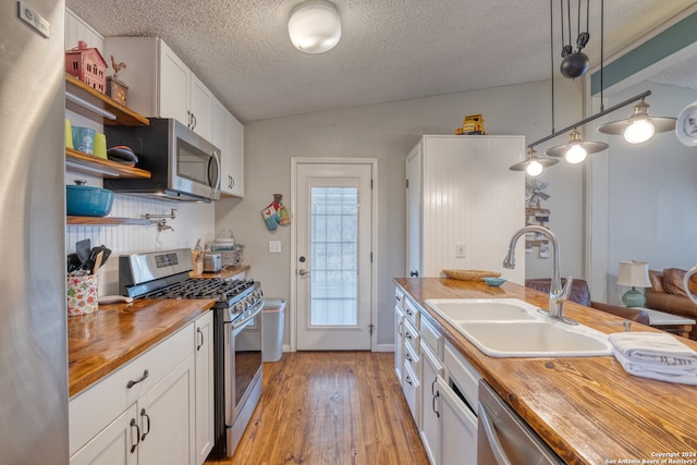 kitchen with wooden counters, sink, appliances with stainless steel finishes, light hardwood / wood-style floors, and pendant lighting