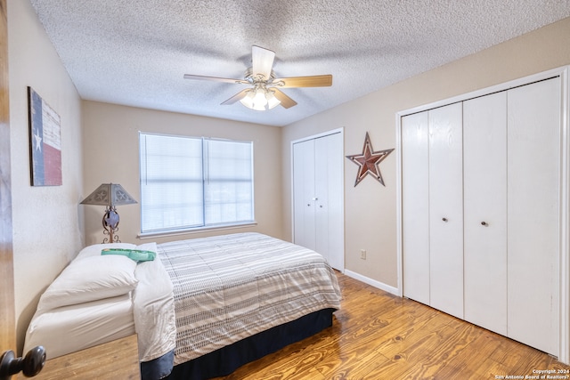 bedroom with ceiling fan, two closets, light hardwood / wood-style flooring, and a textured ceiling