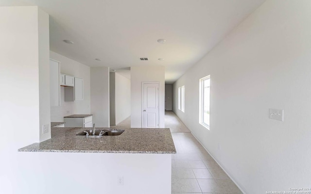 kitchen featuring light stone counters, a sink, white cabinetry, light tile patterned floors, and visible vents