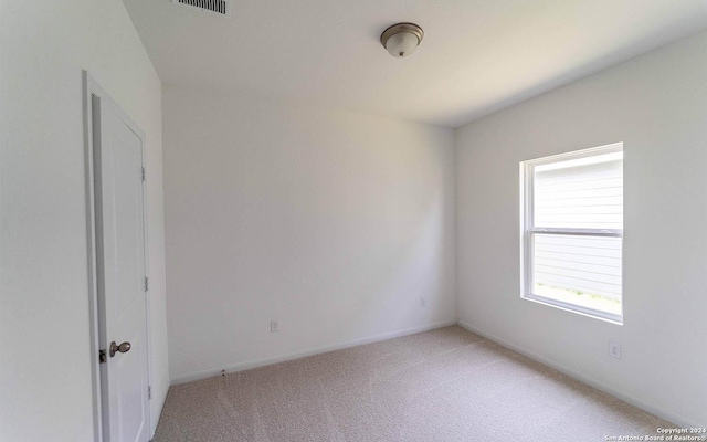spare room featuring baseboards, light colored carpet, and visible vents