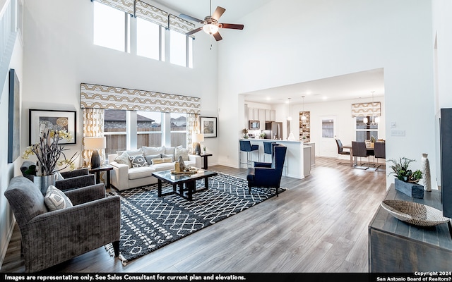 living room featuring a high ceiling, light hardwood / wood-style floors, ceiling fan with notable chandelier, and a wealth of natural light