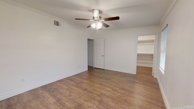 unfurnished bedroom featuring ceiling fan, a walk in closet, crown molding, and dark wood-type flooring