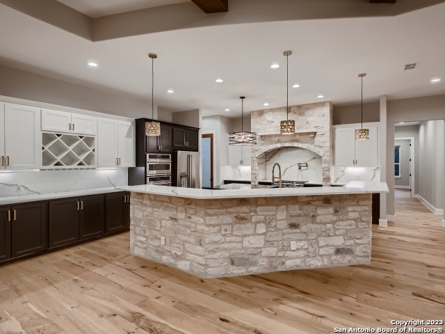 kitchen featuring appliances with stainless steel finishes, light hardwood / wood-style floors, white cabinetry, a kitchen island with sink, and hanging light fixtures