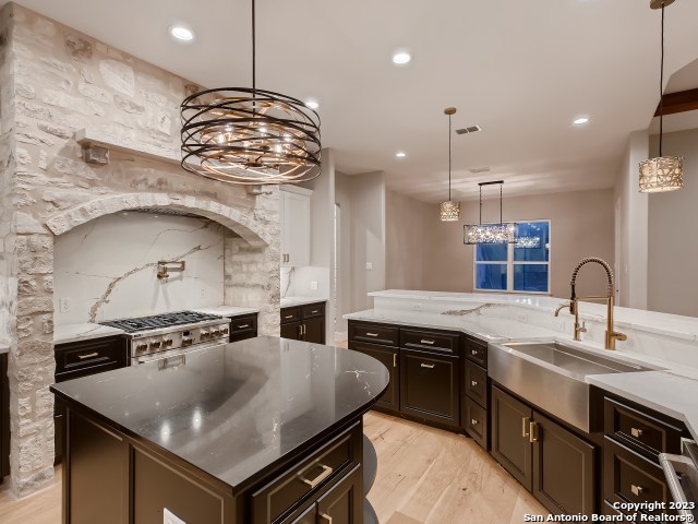 kitchen featuring dark stone counters, an inviting chandelier, light hardwood / wood-style flooring, a center island, and sink