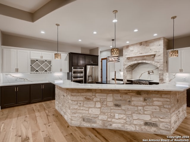 kitchen featuring hanging light fixtures, backsplash, light hardwood / wood-style floors, and stainless steel appliances