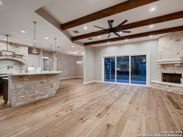 unfurnished living room with beam ceiling, ceiling fan, light wood-type flooring, and a stone fireplace