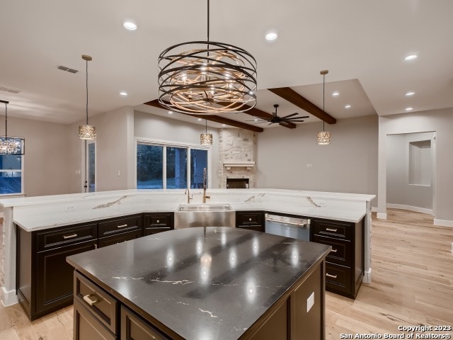 kitchen with stainless steel dishwasher, a stone fireplace, light wood-type flooring, and a center island