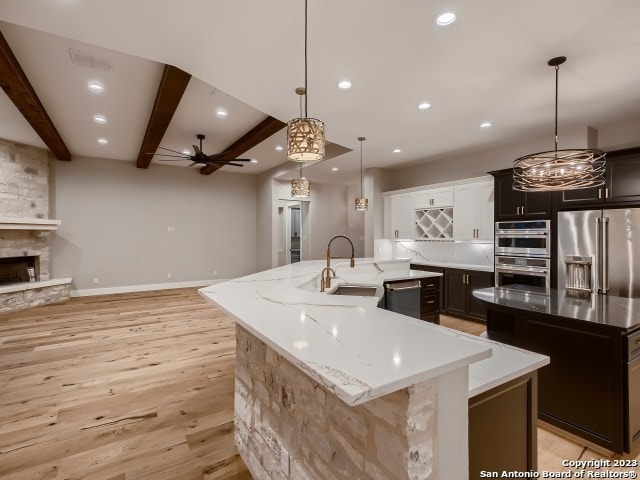 kitchen featuring appliances with stainless steel finishes, hanging light fixtures, ceiling fan, light hardwood / wood-style floors, and a center island with sink