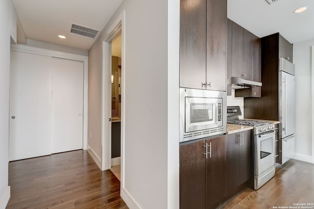 kitchen with tasteful backsplash, dark brown cabinets, built in appliances, and hardwood / wood-style floors