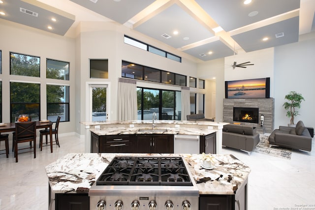 kitchen featuring a kitchen island with sink, sink, light tile floors, light stone counters, and a stone fireplace